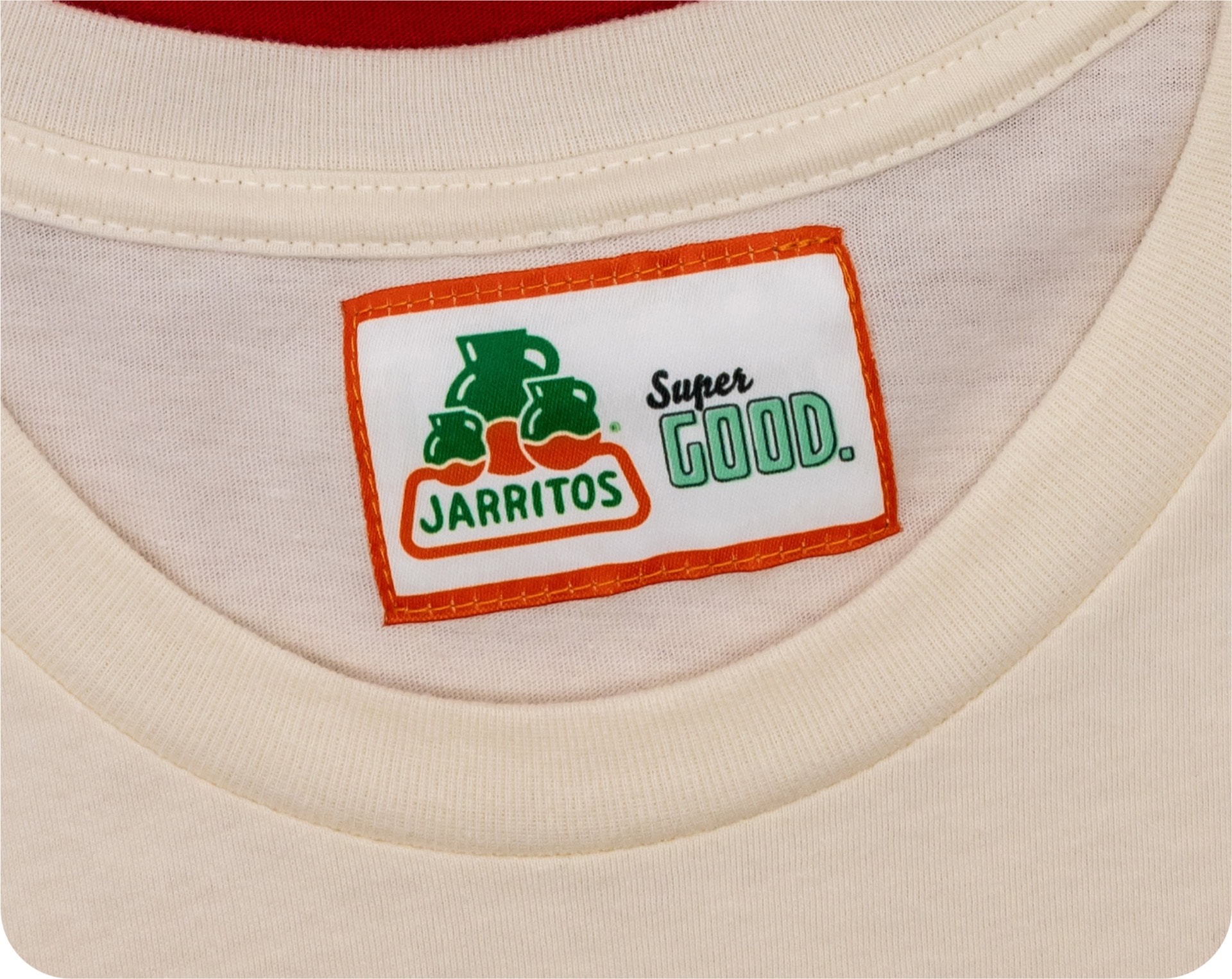 A custom 'JARRITOS Super GOOD' label sewn into the collar of a cream-colored t-shirt.